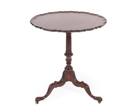 A George III Style Carved Mahogany Tripod Table, the scalloped top above a fluted and carved support, raised on carved and sc