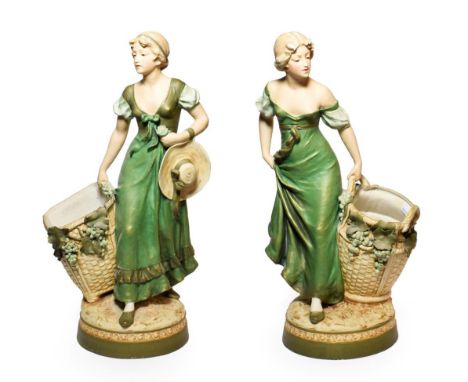 A Pair of Royal Dux Bisque Porcelain Figures of Maidens, early 20th century, loosely dressed carrying basketwork paniers, on 