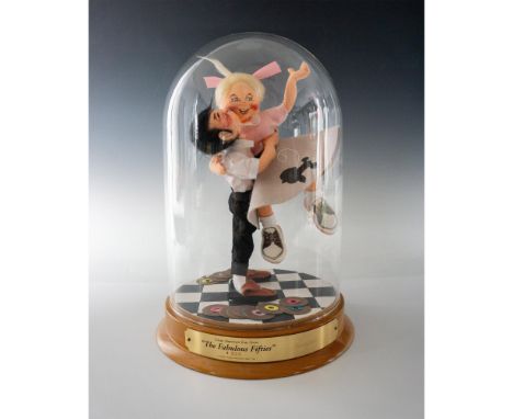 A hand-decorated posable couple dressed in 1950's era clothing fixed on a display base with glass display dome. Signed metal 