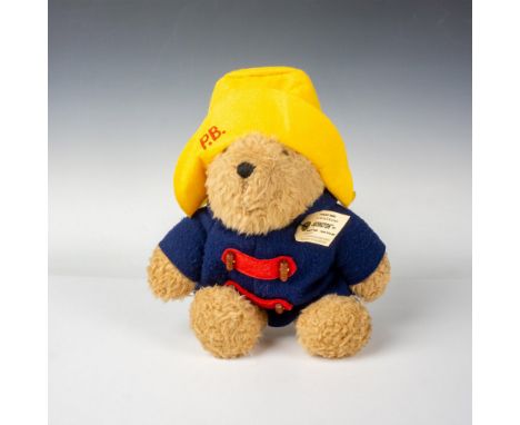 Plush Paddington bear in his blue overcoat with red buttons and bright yellow hat. The tag attached to him asks, Please look 