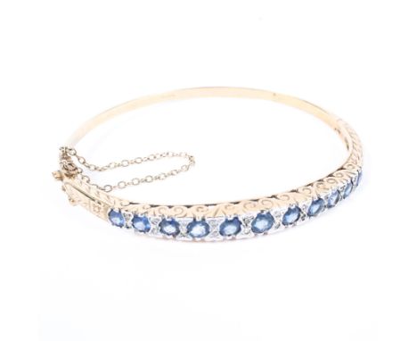 A 9ct gold bangle, half set with a graduated line of eleven round single cut sapphires with illusion set diamond accents, wit