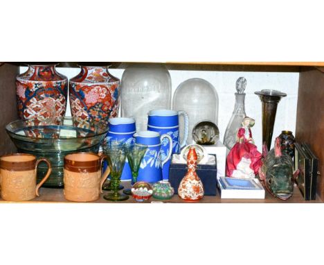 A shelf of ceramics and glass including a pair of Imari vases, two Doulton Lambeth mugs, two glass domes, a Georgian decanter