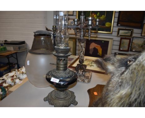 An antique oil burning lamp having ceramic well and brass fitments a wrought iron table lamp and brutalist style candle stem 