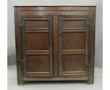 A 17th/18th century panelled oak bacon cupboardThe twin plank rectangular top above twin panelled doors with iron hinges, wit