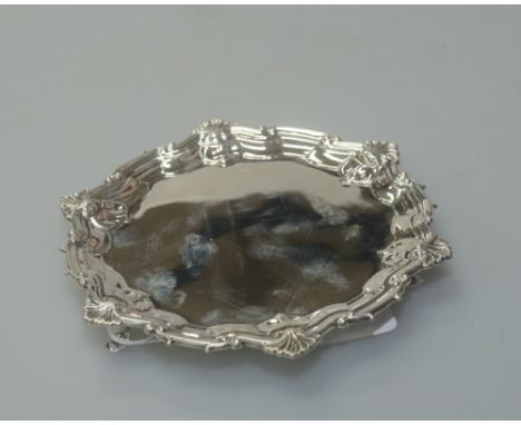 A Victorian silver card tray by Edward Hutton, London 1882, with scroll and shell cast, shaped rim and raised on three pad fe