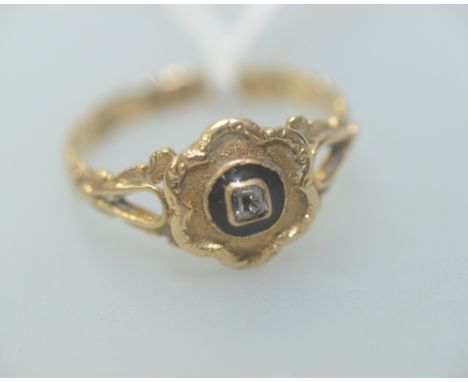 A 19th century 18ct gold mourning ring, with a central diamond surrounded by a ring of enamel on a flower head mount, stamped