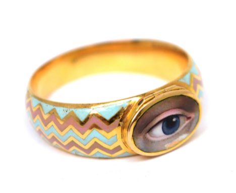 An early 19th century unmarked yellow metal ring with enamel painted eye miniature to top of central hinged compartment and e