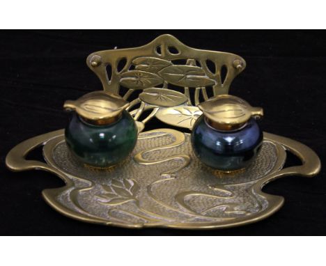 A brass Art Nouveau ink and pen stand with lily pads to the back, two glass and brass inkwells, one in a blue irradescent fin