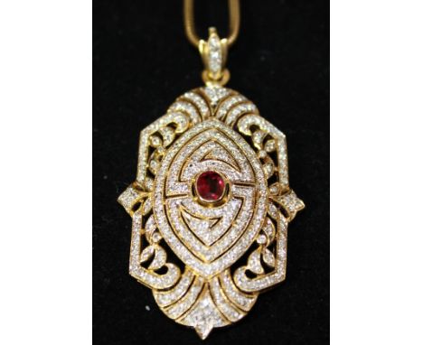 An 18ct gold and diamond shield shaped pendant, the central oval cut ruby within a scrolling foliate setting of approx 200 sm