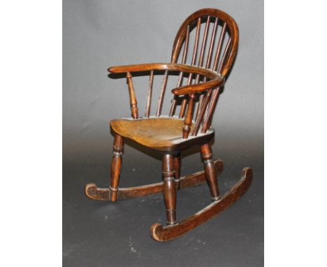 A 19th Century child's yew wood and elm stick back rocking armchair, the shaped seat on baluster turned supports united by C 