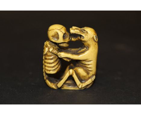 A Japanese carved ivory netsuke as a seated skeleton and wolf embracing, 4.6cm high