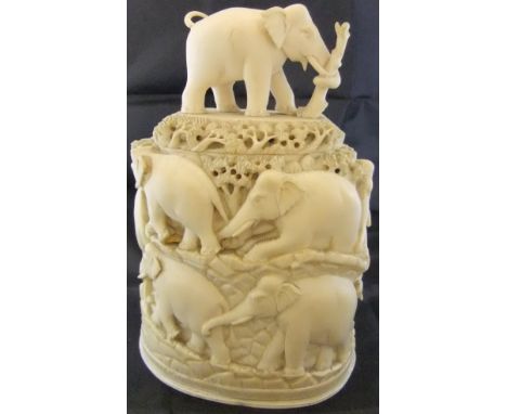 An Indian carved ivory pot and cover decorated with elephants on a mountain roadway, the cover with elephant pulling a tree s