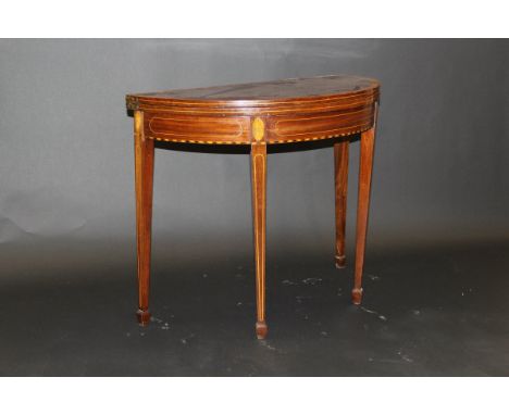 A mahogany crossbanded demi-lune tea table, the sides with shell inlay stringing to square sectioned, tapering legs terminati