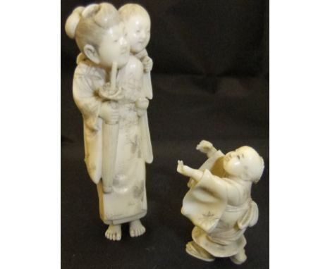 A Japanese Meiji period carved ivory netsuke as a mother with child upon her shoulder, carrying a parasol, bearing signed red