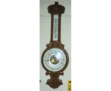 An Edwardian golden oak aneroid barometer with thermometer in carved  case 