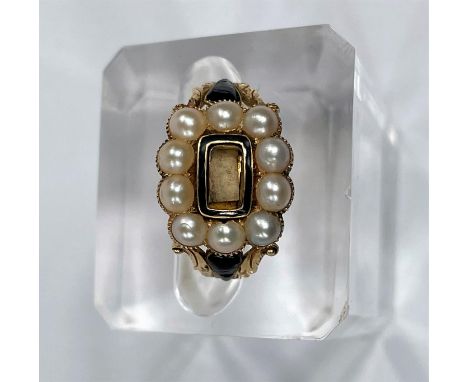 A Victorian 18 carat hallmarked gold mourning ring with ornate decoration in black enamel with seed pearls around the central