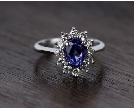 An 18k white gold tanzanite and diamond dress  ring. Central oval free cut Tanzanite 8mm x 6mm with a surround of twelve roun