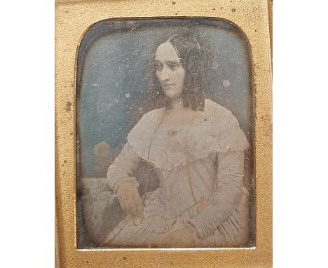 A Daguerreotype portrait of a young woman, mid-19th century, seated three-quarter length, her right arm resting on a table, w