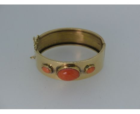 An attractive wide yelow gold hinged Bangle, the front set with three graduated corals and with a pin fastening clasp, unmark