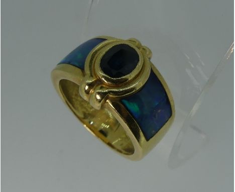 A wide 18kt yellow gold Ring, set in the front with a facetted oval dark sapphire, within a gold border and opal doublet shou