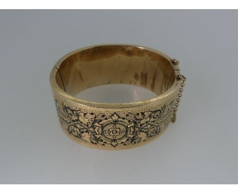 A yellow metal hinged Bangle, textured throughout with black foliate decoration, unmarked but tested as gold, 43g