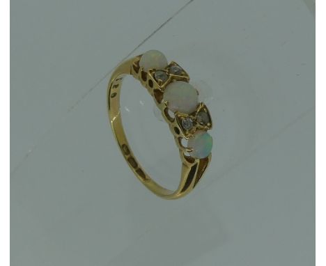 A graduated three stone opal Ring, the central stone with two diamonds set between, all mounted in 18ct yellow gold, Size M.