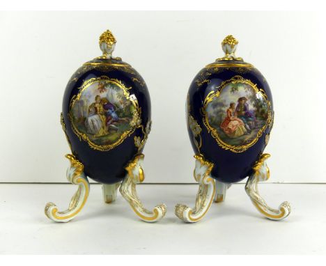 A pair of 19th Century hand painted lidded urns
Of ovoid form, raised on three scrolling legs, possibly Meissen, each decorat