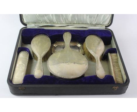 A 1960s silver dressing table setComprising a hand mirror, two brushes and a comb all with engine-turned detailing, within a 