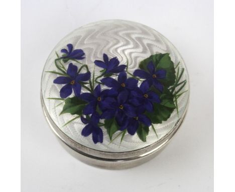 An Edwardian silver enamel pill boxOf circular outline, with white guilloche enamel lid painted with purple flowers to the si