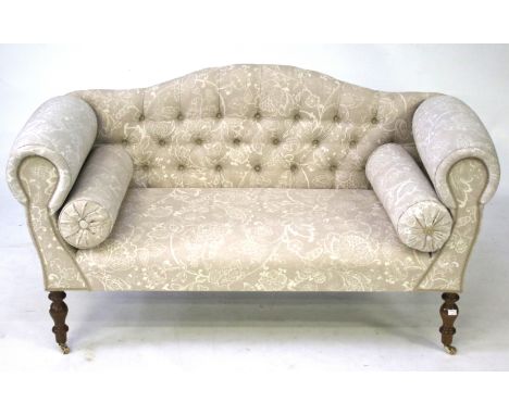 A small two seater button back sofa. Upholstered in grey floral fabric, raised on turned supports, with casters, H77cm x W134