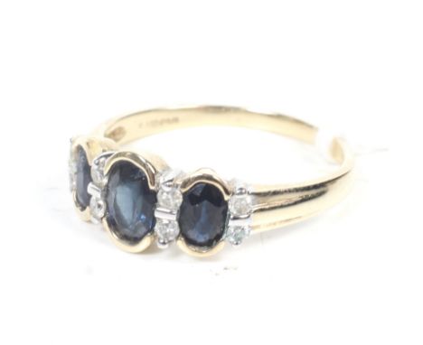 A modern 9ct gold, sapphire and diamond dress ring. The three graduated oval mixed-cut sapphires each flanked by pairs of sma