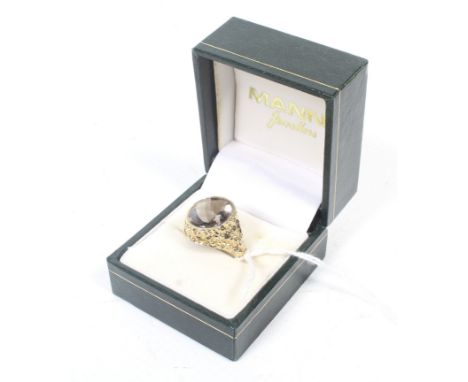 A 9ct gold and oval citrine single stone ring. The oval mixed-cut stone rub-over set within a bark-textured gallery on a D-se