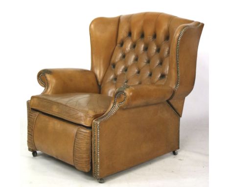 A vintage tan leather reclining button back armchair. With brass studded scroll arms on casters. L82cm x D77cm  x H90cm