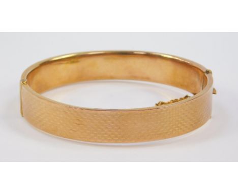 A 9ct gold bangle, with edge and turned decoration, on a snap clasp with safety chain as fitted, 12.4g.