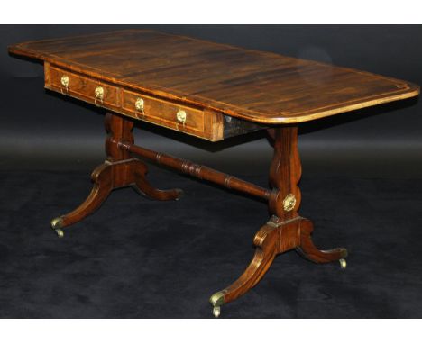 A Regency rosewood sofa table, the rounded rectangular drop-leaf top with satinwood banding over two frieze drawers with lion