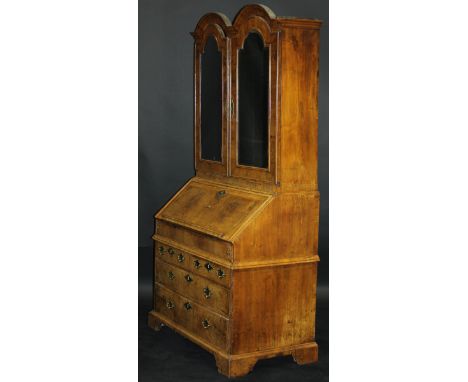 An early 18th Century walnut bureau cabinet, the double arched top with moulded cornice over two bevelled mirror plate doors,