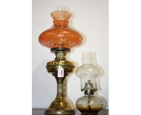 An early 20th century brass pedestal oil lamp, having an orange tinted glass shade; together with one other smaller example (