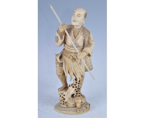 A Japanese Meiji period (1868-1912) ivory okimono, carved as a spear fisherman in standing pose with trident in hands and a b