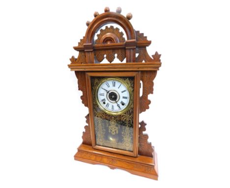 A late 19thC American mantel clock, in gingerbread style walnut case, with pierced crest, above a gilt verre eglomise door, t