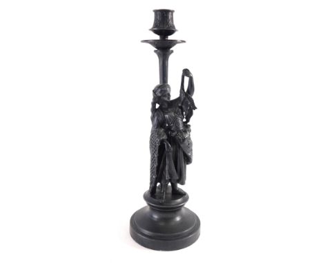 A spelter candlestick, elaborately decorated, with shaped dish holder on shaped stem, fronted by a figure dressed in finery, 