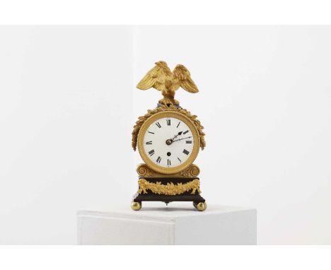 A French Empire mantel timepiece,the drum shaped case seated on an ormolu scrolled base with an enamel dial within an engine-