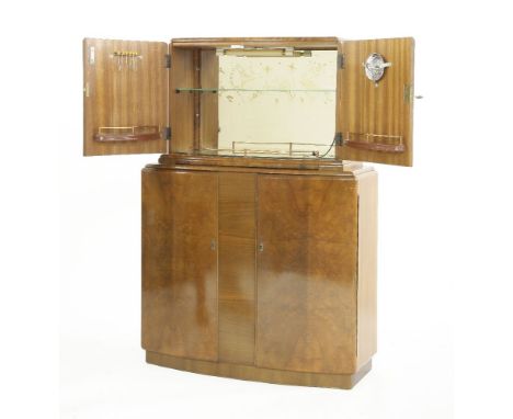 A walnut two-tier cocktail cabinet,the top with a mirror back and shaped glass back, with a shelf over a further cupboard, ce