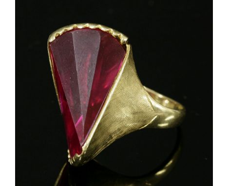 A gold, synthetic ruby ring, c.1960,with a tapering wedge-shaped synthetic ruby, with tapering stepped facets, claw set at ea