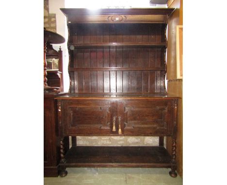 An Edwardian oak dresser and plate rack in the Jacobean style, the base enclosed by two panelled doors over an open shelf wit