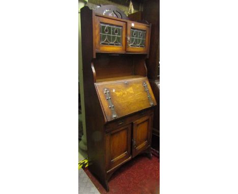 An arts and crafts style slim bureau cabinet, the upper section with pierced fretwork detail partially enclosed by a pair of 