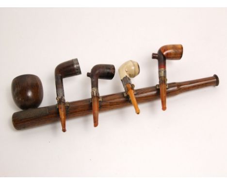 An oak wall mounted pipe rack in the form of a pipe - securing four pipes, all with silver mounts