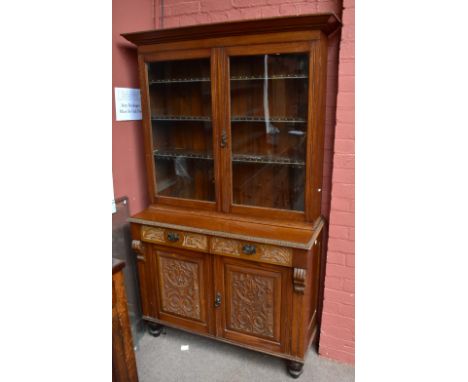 A late Victorian carved oak bookcase, with two glazed doors enclosing adjustable shelves above two drawers and two cupboard d