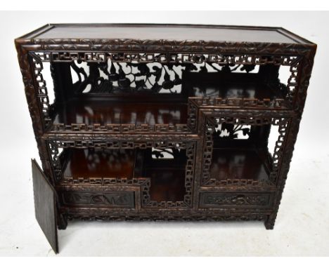 A Chinese carved hardwood low display cabinet, with two drawers above an arrangement of two shelves, with pierced fretwork de