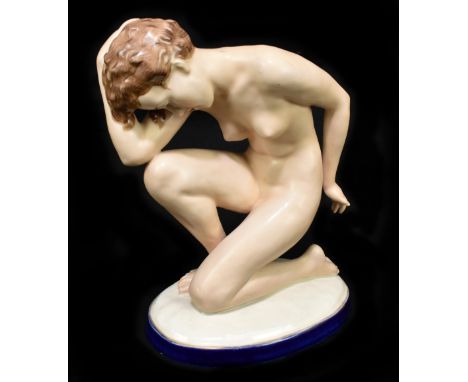 An Art Deco Czechoslovakian ceramic figure (possibly Royal Dux), modelled as a nude maiden kneeling on an oval plinth base, p