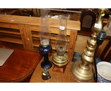 A blue glass oil lamp with glass chimney; a brass oil lamp with glass chimney; and a Wells Unbreakable house lamp